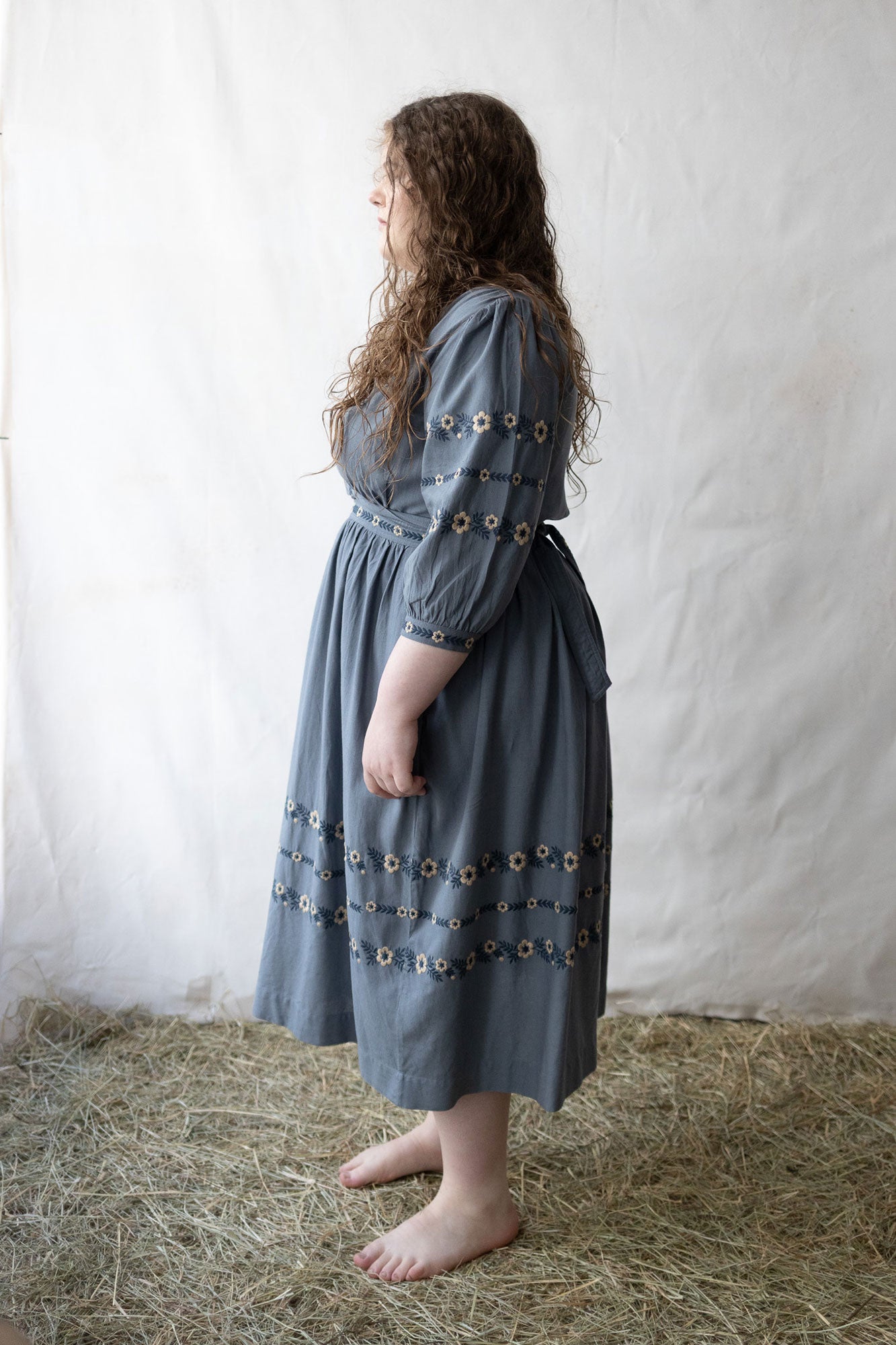 Plussize woman wearing a blue dress with floral details against a plain background