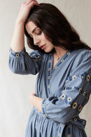 Woman wearing a crossover blue dress with floral embroideries.