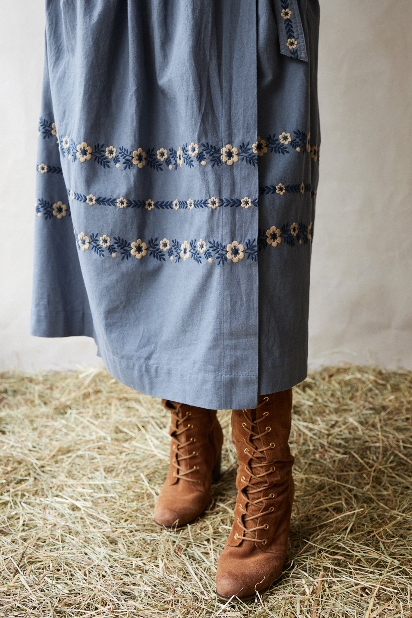 Blue dress with floral embroidery and brown boots on a straw surface