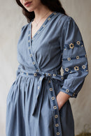 Woman wearing a crossover blue dress with floral embroideries standing on hay.