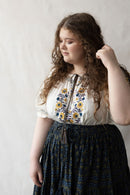 + size Woman wearing a white Hungarian Matyo blouse with floral embroidery against a plain background
