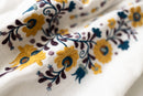 Close-up of floral Matyo embroidery on fabric with yellow flowers and brown leaves.