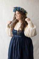 Woman plus size in a blue dress with floral crown against a plain background