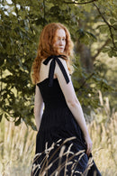 Woman in a black dress with a bow standing in a natural setting