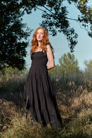 Woman in a black dress standing in a field with trees in the background