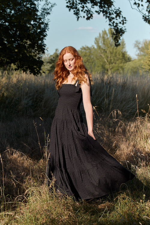 Woman in a black dress standing in a field with trees in the background