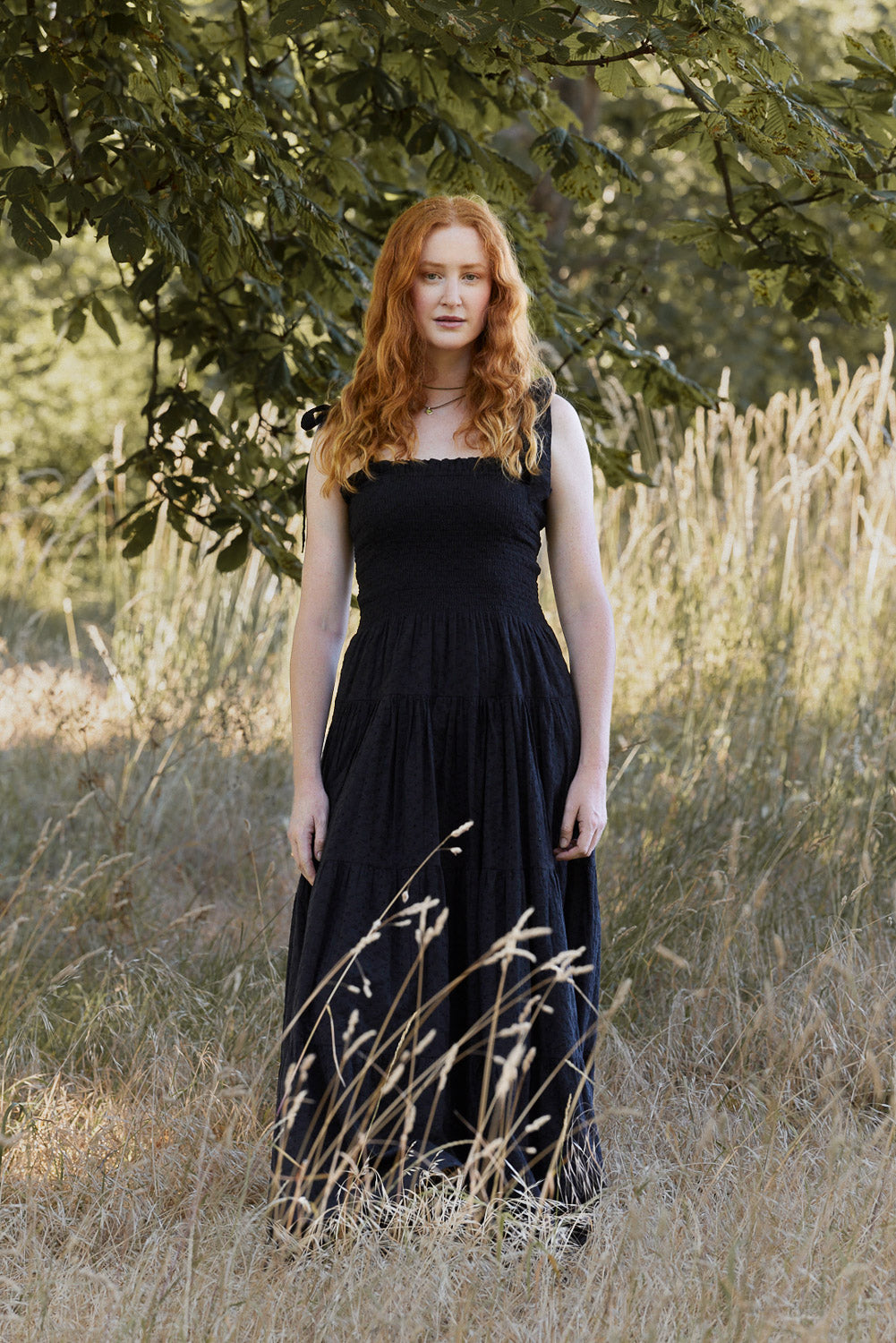 Woman in a black dress standing in a field with trees in the background
