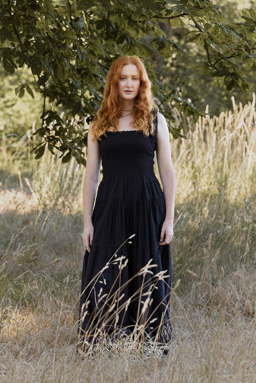 Woman in a black dress standing in a field with trees in the background