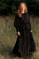 Woman in a black dress standing in a field with trees in the background