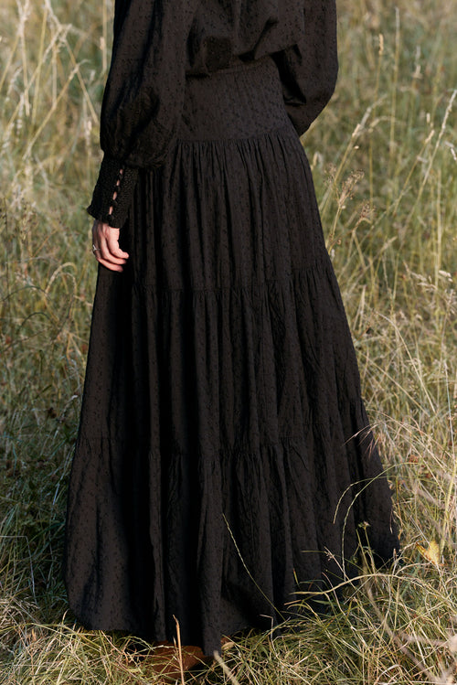 Person wearing a long black dress standing in a grassy field