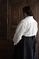 Person wearing a white shirt and dark skirt standing in front of a wooden door.