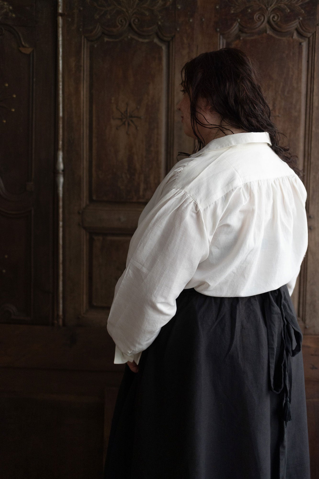 Person wearing a white shirt and dark skirt standing in front of a wooden door.