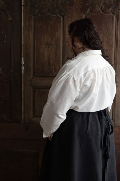 Person wearing a white shirt and dark skirt standing in front of a wooden door.