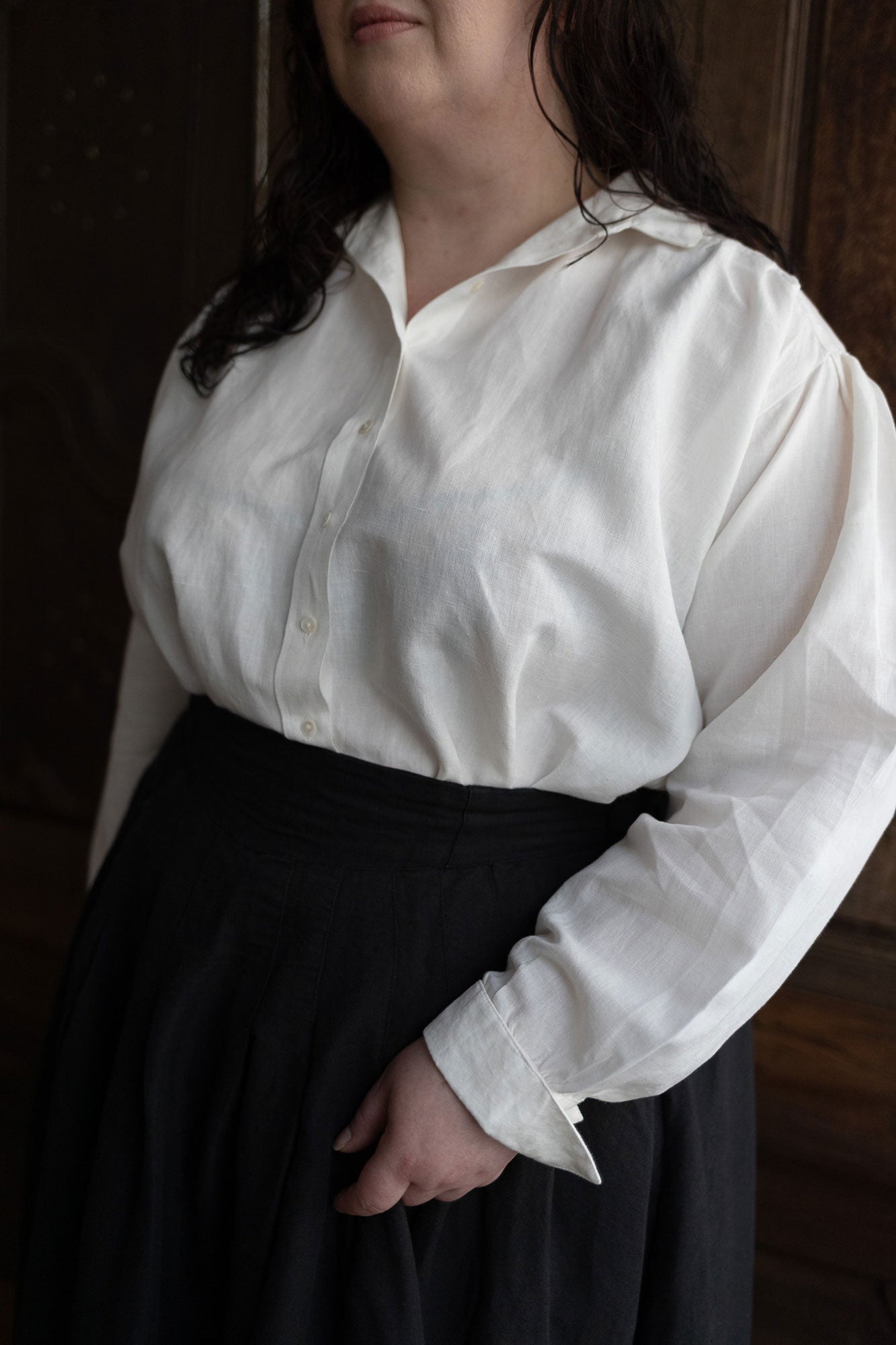 Person wearing a white blouse with long sleeves and a black skirt in a dimly lit room.