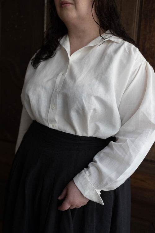 Person wearing a white blouse with long sleeves and a black skirt in a dimly lit room.