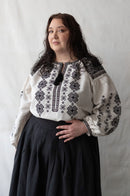 Woman plus size wearing a white blouse with black embroidery against a plain background