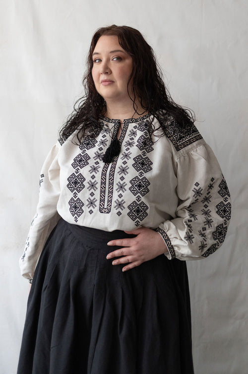 Woman plus size wearing a white blouse with black embroidery against a plain background