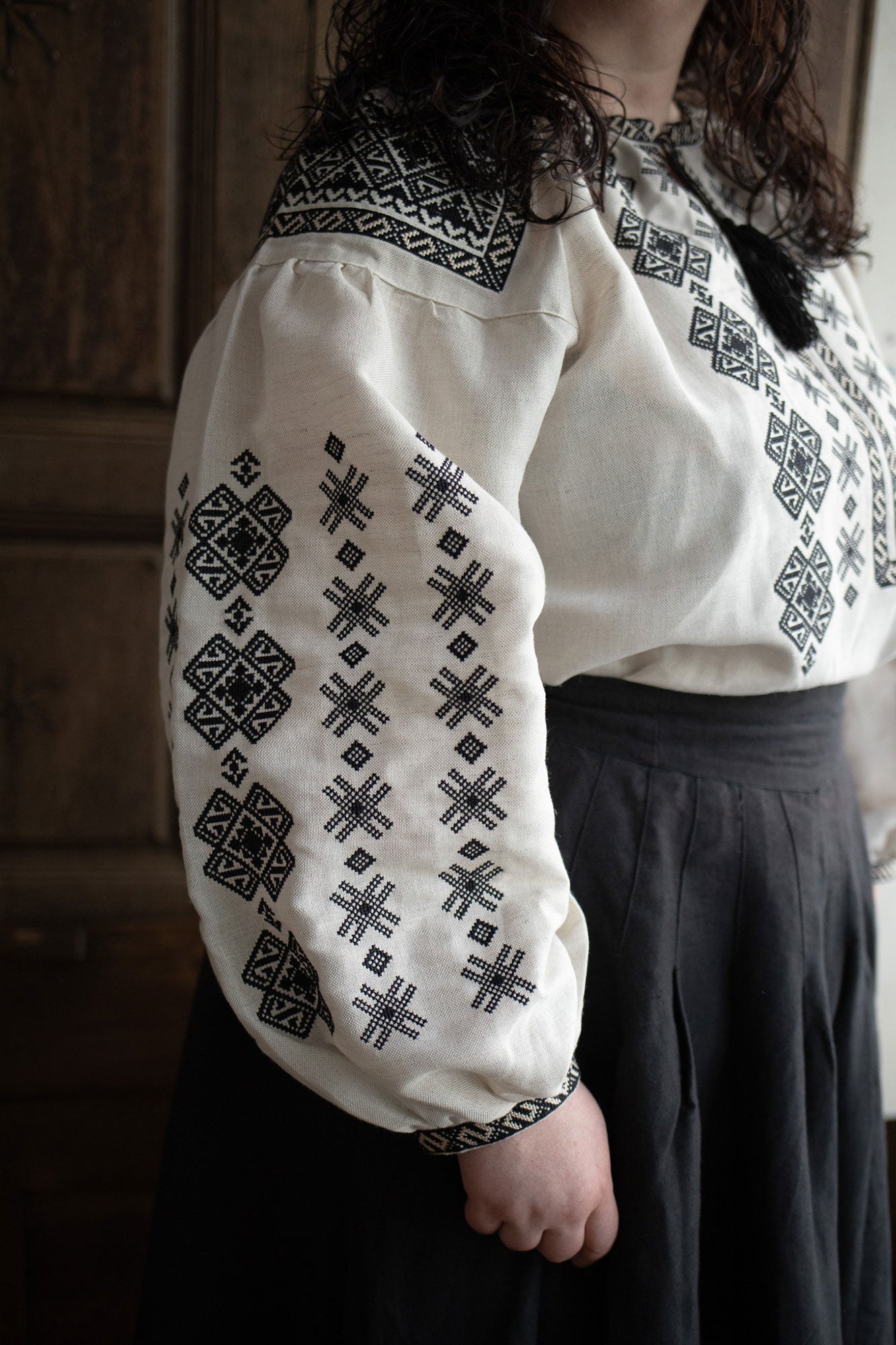 Woman plus size wearing a white blouse with black embroidery against a plain background