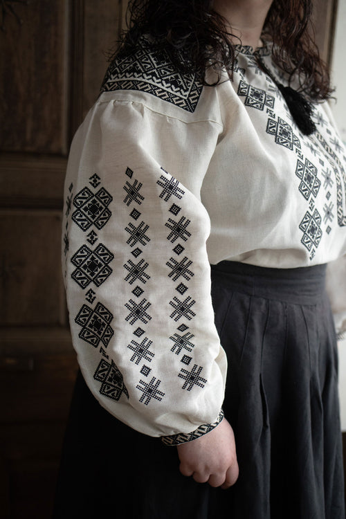 Woman plus size wearing a white blouse with black embroidery against a plain background