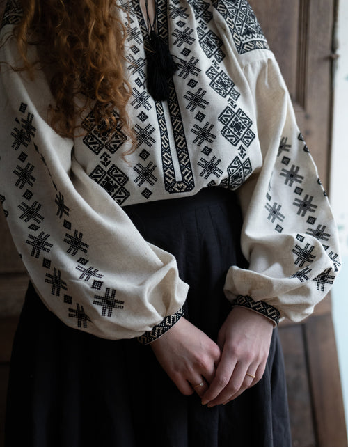 Person wearing a traditional embroidered blouse with a dark background