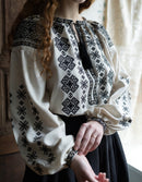 Person wearing a white blouse with black geometric patterns in a softly lit room.