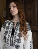 Woman wearing a white blouse with black geometric patterns in a warm-toned room.