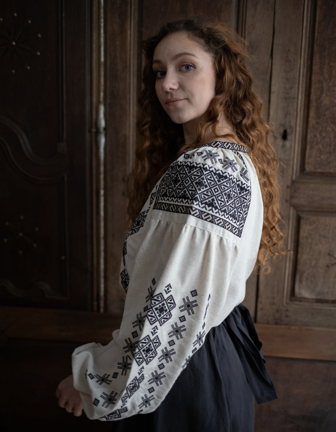 Woman wearing a white blouse with black embroidery in a rustic setting