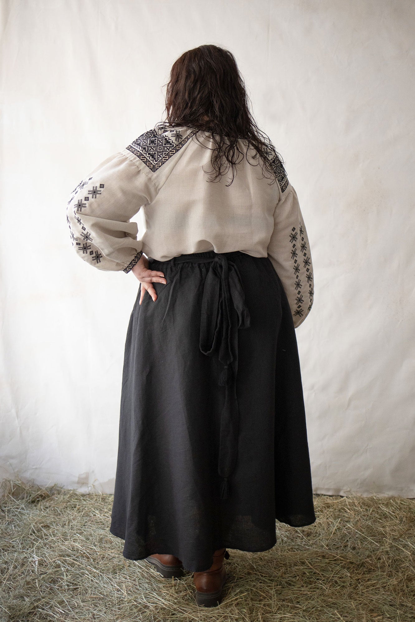 Woman plus size wearing a white blouse with black embroidery against a plain background