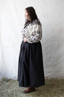 Woman plus size wearing a white blouse with black embroidery against a plain background