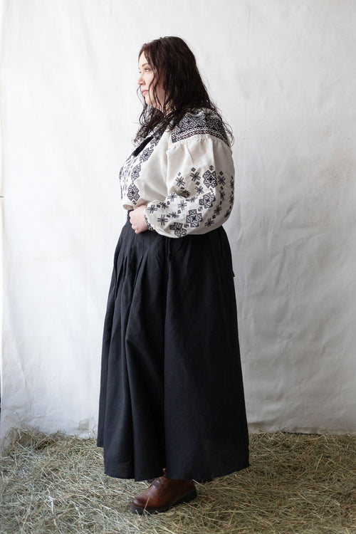 Woman plus size wearing a white blouse with black embroidery against a plain background