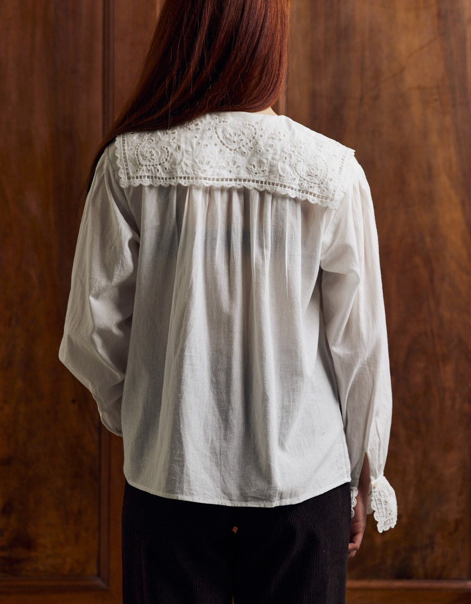 Person wearing a white blouse with lace collar against a wooden background