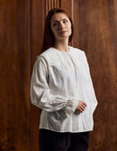 Woman wearing a white blouse with lace details against a wooden background