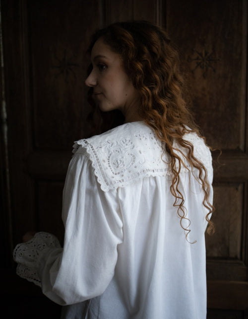 Woman wearing a white blouse with lace details in a dimly lit room.