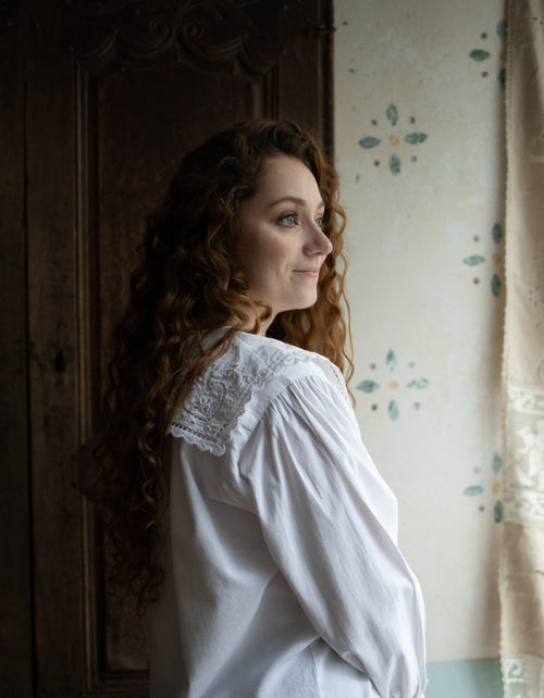 Woman in a white blouse standing in a room with floral wallpaper