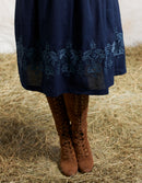 Navy blue dress with intricate patterns worn by a person standing on hay.