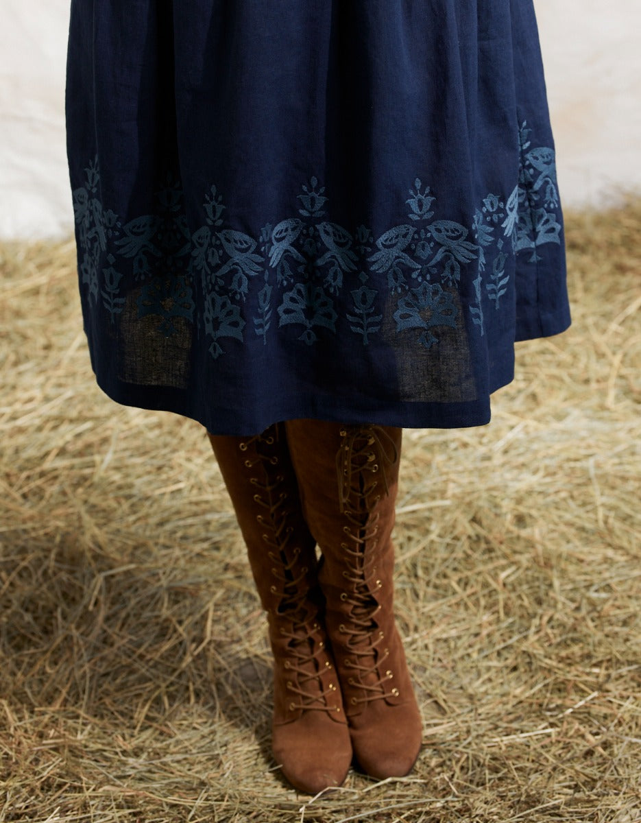 Navy blue dress with intricate patterns worn by a person standing on hay.