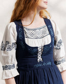 Person wearing a traditional Bunad embroidered dress with a white blouse and blue apron.
