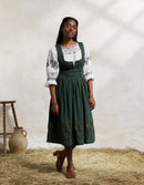 Woman wearing a traiditonal green Bunad dress with a white blouse in a rustic setting