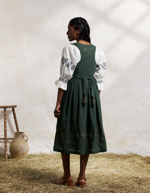 Woman wearing a traiditonal green Bunad dress with a white blouse in a rustic setting