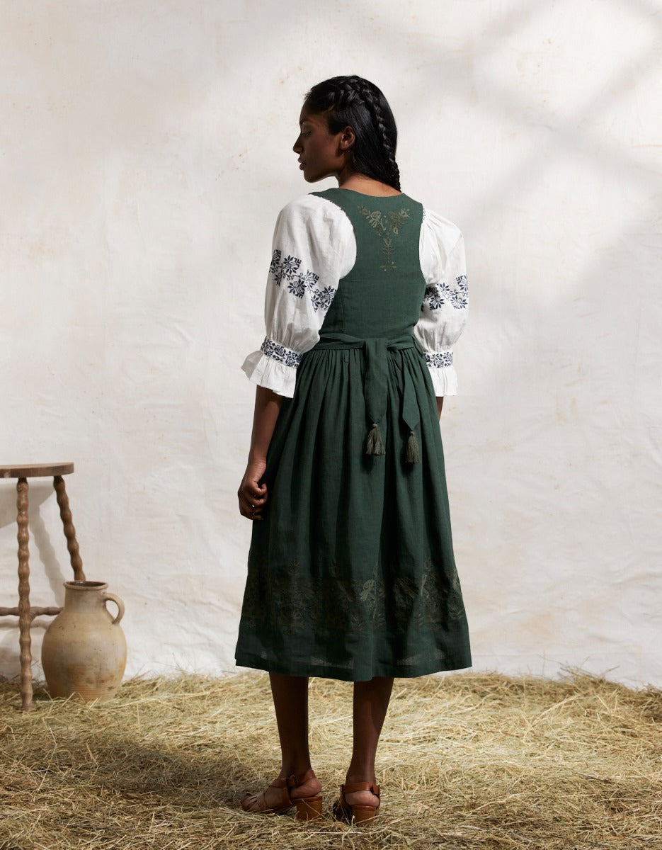 Woman wearing a traiditonal green Bunad dress with a white blouse in a rustic setting