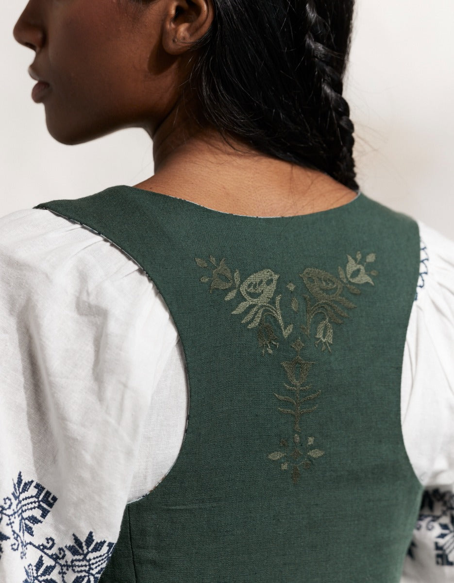 Woman wearing a traiditonal green Bunad dress with a white blouse in a rustic setting
