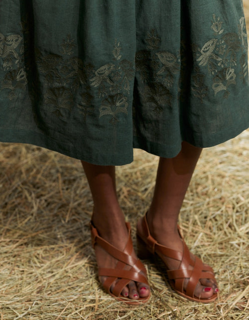 Woman wearing a traiditonal green Bunad dress with a white blouse in a rustic setting