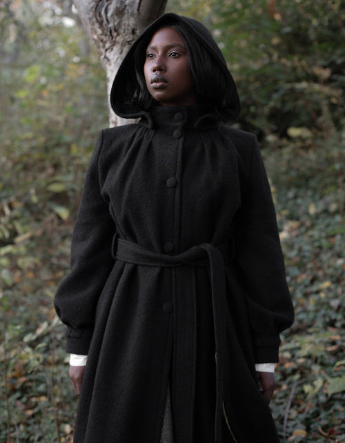 Person wearing a black hooded coat standing in a forest setting