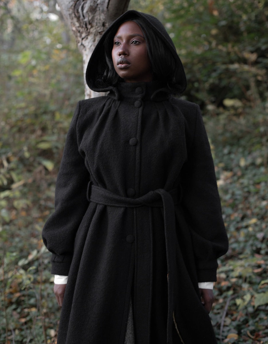 Person wearing a black hooded coat standing in a forest setting