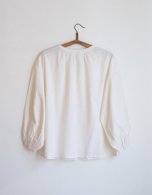 White blouse on a wooden hanger against a white background