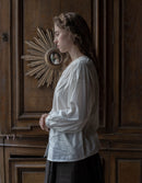 Woman in a white blouse standing in front of a wooden wall with decorative elements