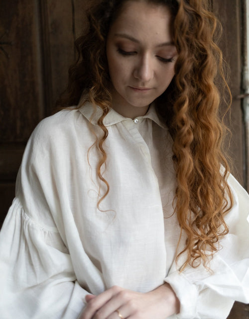 Woman wearing a white blouse with long, wavy hair against a wooden background