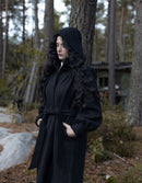 Person wearing a black coat with a hood in a forest setting
