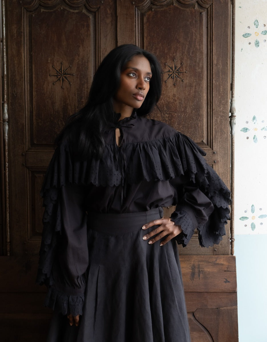 Woman wearing a black ruffled top and skirt standing in front of a wooden door.