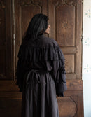 Person wearing a dark layered dress standing in front of a wooden door.